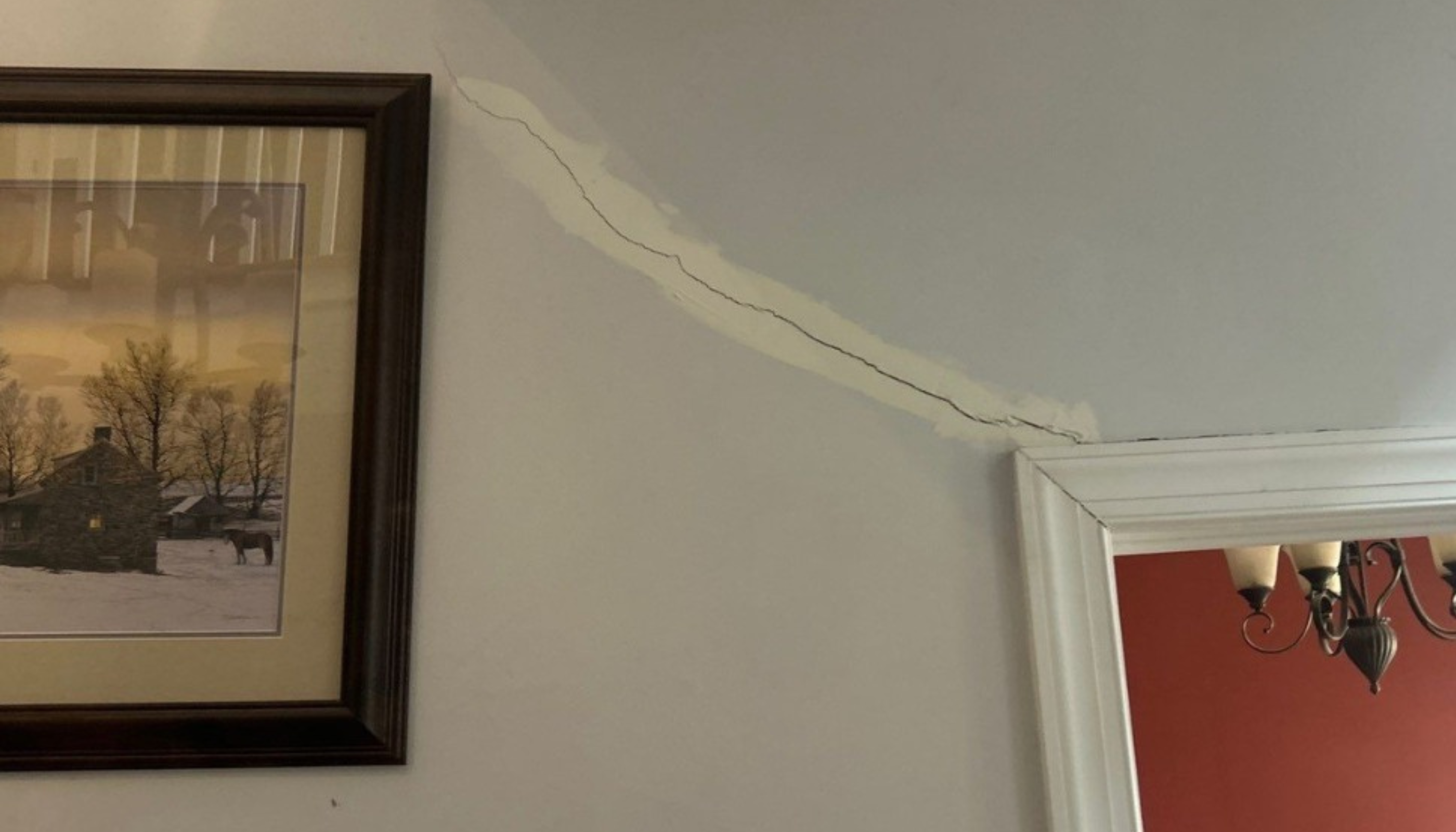 Crack in wall of home with pastoral painting on left and dining room on right