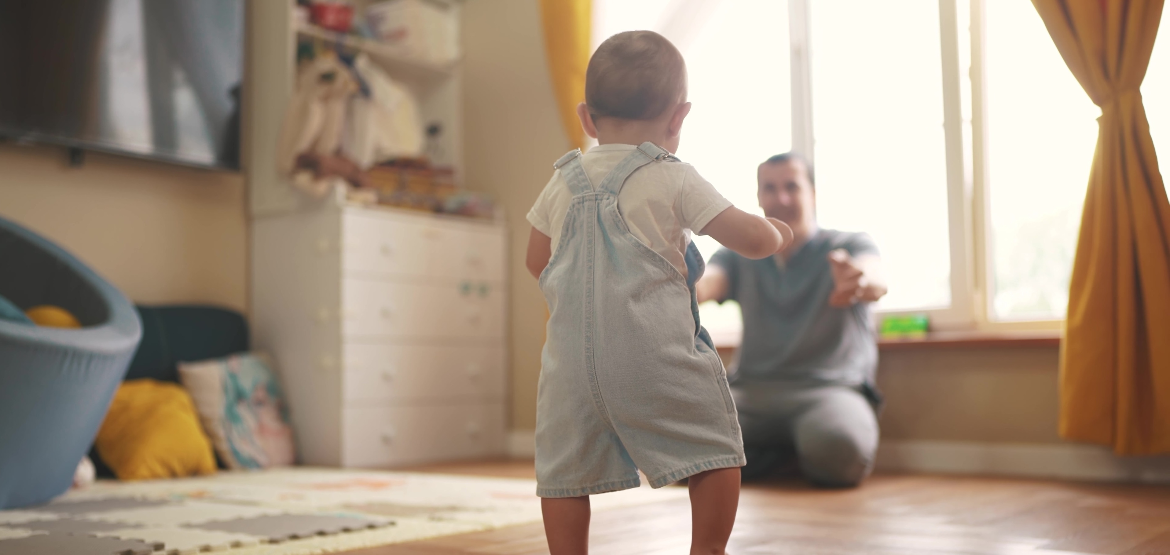 baby walking to dad in a living room