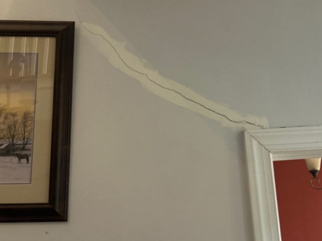 Crack in wall of home with pastoral painting on left and dining room on right