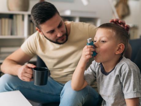 Young boy using inhaler during asthma attack while father comforts him